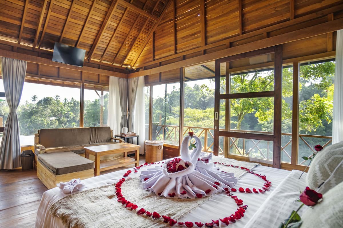 A wooden cabin with a bed, a sofa, and a table. There are large windows and a balcony.