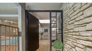 Un intérieur moderne avec un mur en pierre, un plancher en bois, une porte noire et une vue sur une piscine.