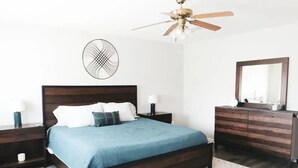 Ein Schlafzimmer mit Bett, Nachttischen, einem Schminktisch und einer Wanddekoration sowie einem Deckenventilator.