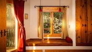Una habitación con suelo de madera, una ventana con cortinas, una lámpara roja y una puerta de madera.