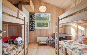 A wooden cabin with bunk beds, a small desk, and a window with curtains.