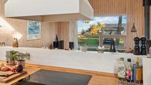 Eine moderne Küche mit Holzwänden, einem großen Fenster und Blick auf ein Haus und Bäume.