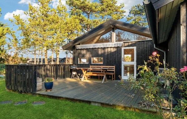 A wooden cabin with a deck, a bench, and a barbecue grill.