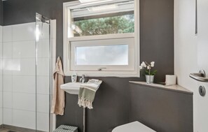 A bathroom with a shower, a sink with a towel, a window, and a small plant.