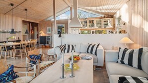 Ein gemütliches, helles Wohnzimmer mit Holzbalkendecke, einem Essbereich mit Tisch und Stühlen sowie einer Küche mit Schränken und einem Fenster.