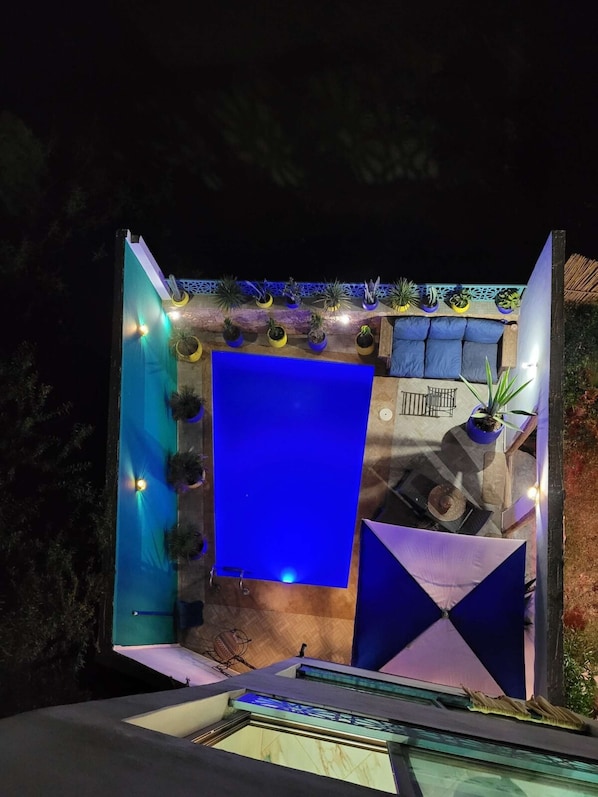 A modern outdoor seating area with a blue partition, potted plants, and ambient lighting.