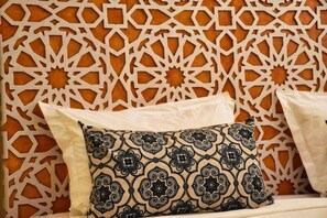 A room with a patterned wall, a bed with white bedding, and a decorative pillow with a geometric design.