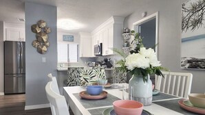 Eine moderne Küche mit weißen Schränken, einem Edelstahl-Kühlschrank und einem Essbereich mit Tisch für vier Personen.