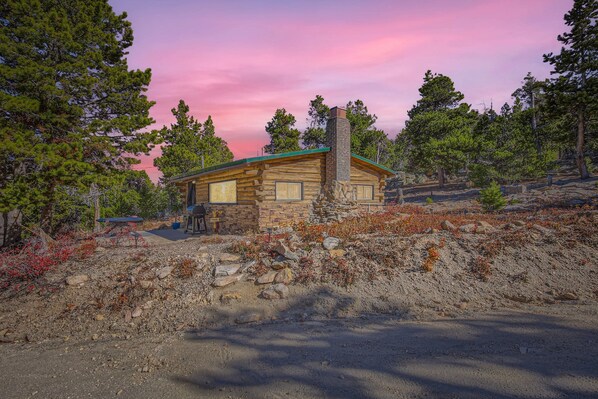 A log cabin with a stone foundation, surrounded by trees and a dirt path. - Secluded log cabin/hot tub. Ski, views, hike, silence. (Black Hawk)
