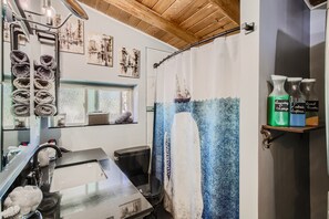 A bathroom with a sink, toilet, and a shower curtain with a nautical design. There are towels hanging on a rack, and a shelf with bottles of laundry products. - Secluded log cabin/hot tub. Ski, views, hike, silence. (Black Hawk)