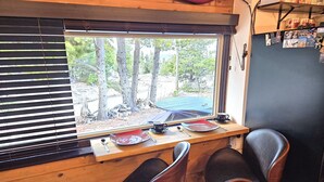 Ein gemütliches Blockhaus-Interieur mit einem Holztisch, gedeckt für zwei Personen, einem Fenster mit Jalousien und einer Wand mit verschiedenen Dekorationen.