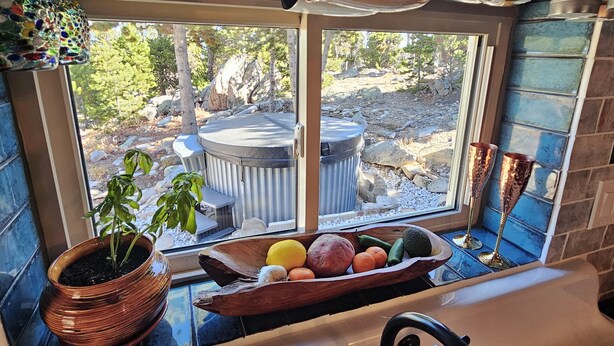Eine Küche mit Fensterblick auf ein Whirlpool und eine Außenanlage, einer Topfpflanze sowie einer Holzküche mit Obst und Gemüse.
