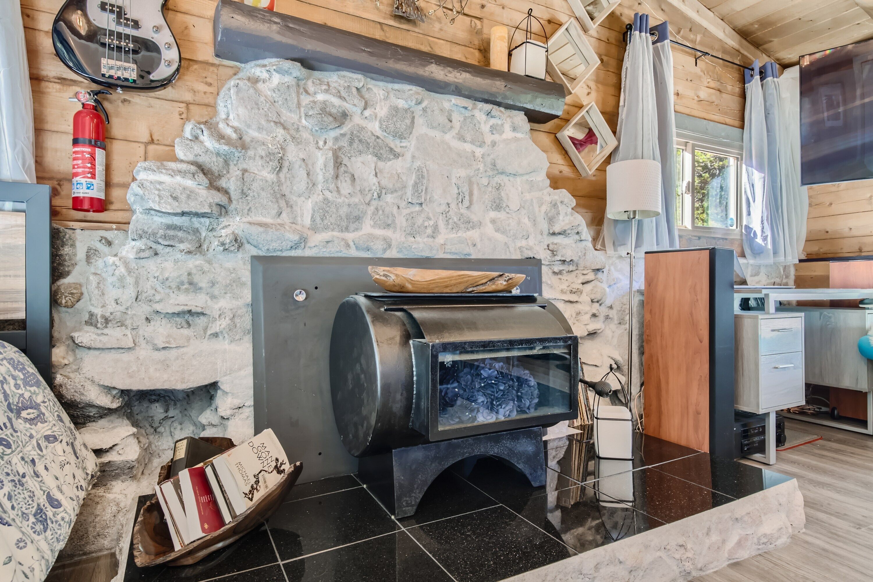Ein gemütliches Blockhäuschen-Interieur mit Kamin aus Stein, Holzbalkendecke und kleiner Küchenzeile.