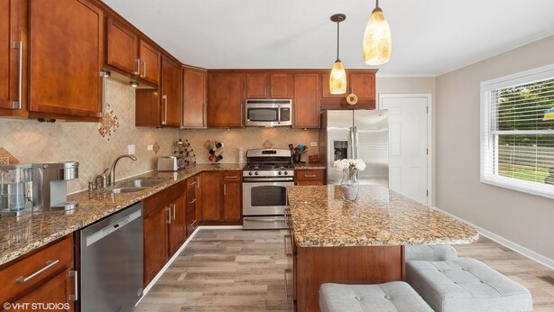 A modern kitchen with wooden cabinets, granite countertops, stainless steel appliances, and pendant lighting. - Single Family home in Schaumburg, IL 3 bed/ 2 full baths/ fully fenced backyard (Schaumburg)