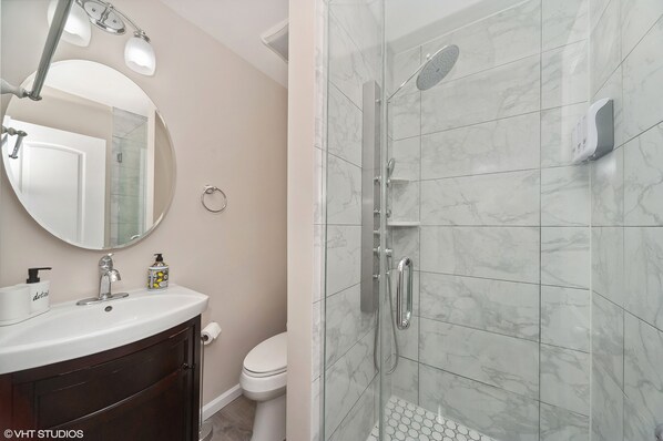 A bathroom with a white sink, mirror, and toilet, and a glass-enclosed shower area with a marble floor.