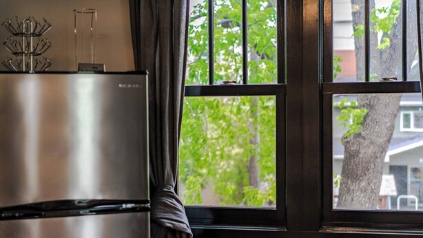 A kitchen with a stainless steel refrigerator, a window with a view of trees, and a curtain. - Historical Building 1br 1ba Walk To Roger's Place (Edmonton)