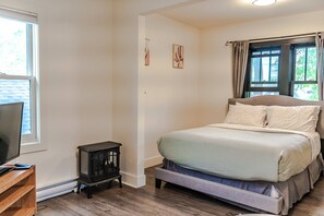 Relax in this serene bedroom with a large bed, nightstand, and TV, surrounded by framed artworks and natural light.