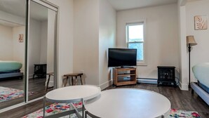 A bedroom with a bed, a TV, a small table, a window, and a mirror. - Historical Building 1br 1ba Walk To Roger's Place (Edmonton)