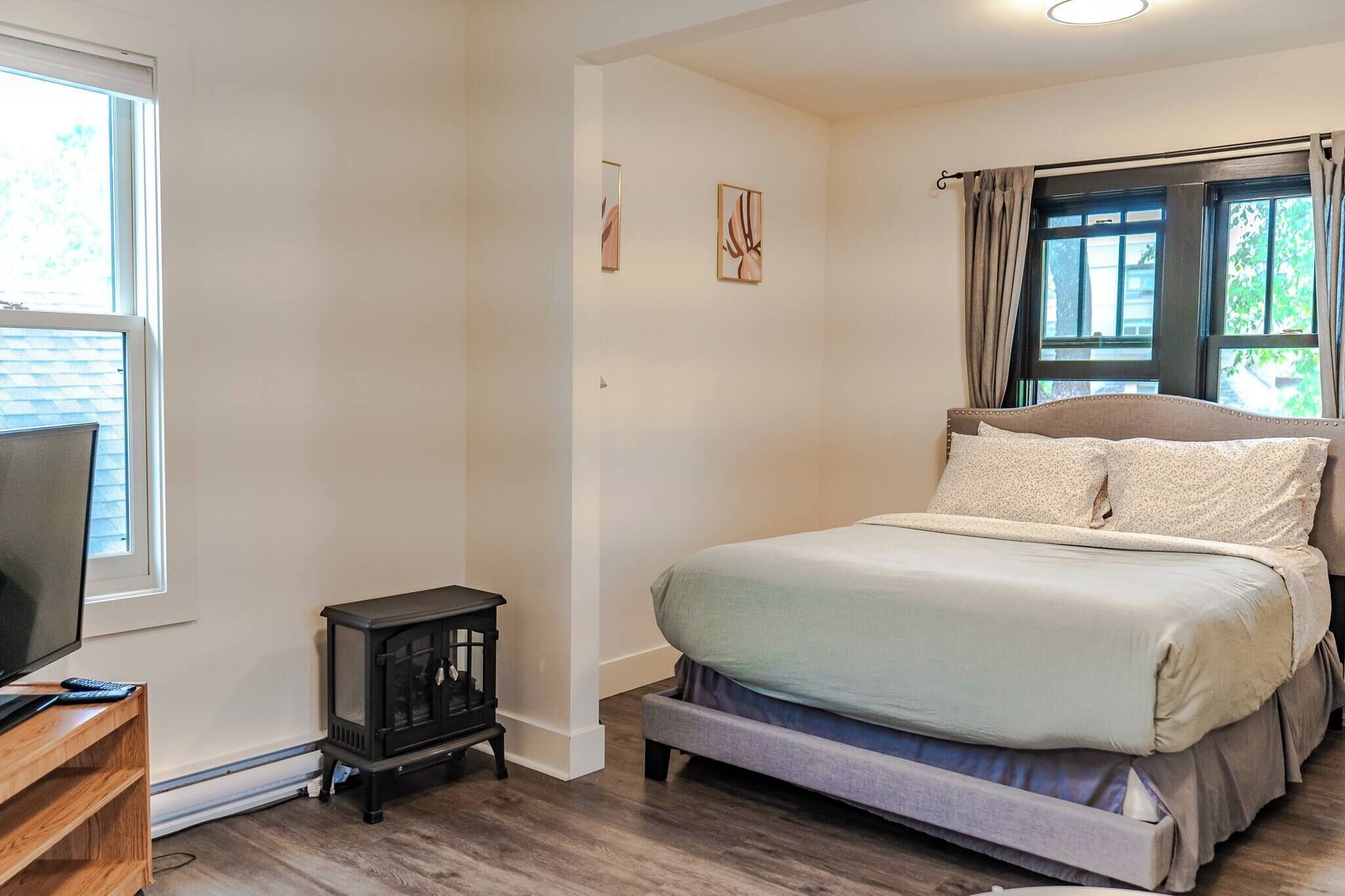 A bedroom with a bed, a television, a small cabinet, and a window with curtains.