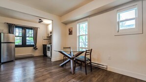 A kitchen with a dining table and chairs, a refrigerator, and a window with curtains. - Historical Building 1br 1ba Walk To Roger's Place (Edmonton)