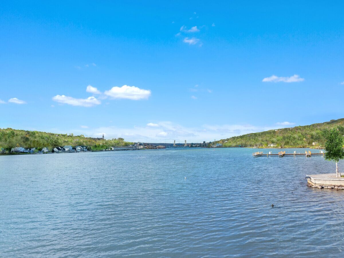 Un lago tranquilo con un muelle y un pequeño árbol a la derecha.