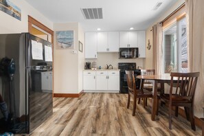 Une cuisine avec des meubles blancs, un réfrigérateur, un four à micro-ondes et un coin repas avec des chaises en bois.