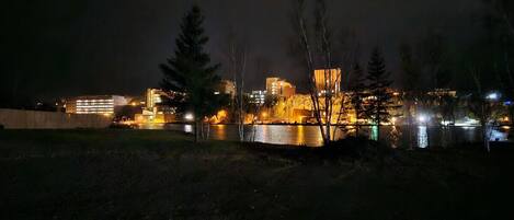 Nachts beleuchtete Stadtansicht mit Gebäuden und einem Fluss.