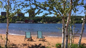 Une vue sur le lac, avec deux chaises vertes posées sur le sable, entourées de bouleaux.