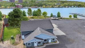 Un bâtiment à deux étages, doté d’un toit en pente, d’un espace de stationnement et offrant une vue sur un lac avec un quai et des bateaux.