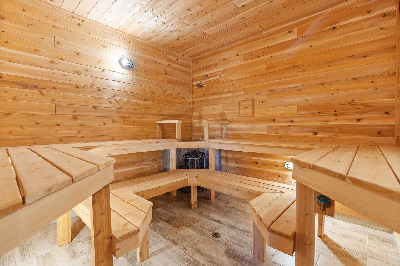 A sauna room with wooden benches arranged in a semi-circle, a central heating element, and a metal grate at the bottom.