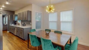 A modern kitchen with grey cabinets, a wooden dining table, and teal chairs. - Prohibition Vibes | LUX | Mini Golf | Walk to AT&T (Arlington)