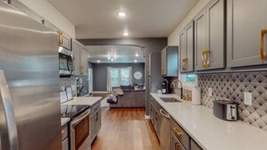 A modern kitchen with stainless steel appliances, a central island, and a view into the living area. - Prohibition Vibes | LUX | Mini Golf | Walk to AT&T (Arlington)