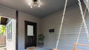 A porch with a swing chair, a door, and a small potted plant. - Prohibition Vibes | LUX | Mini Golf | Walk to AT&T (Arlington)