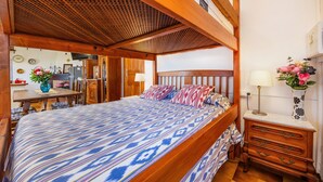A bedroom with a wooden bed, a nightstand, a lamp, and a vase with flowers.