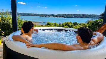 Two individuals in a hot tub with a scenic view of a lake and hills.