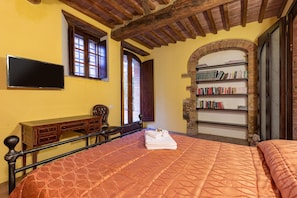 A bedroom with a bed, a desk, a bookshelf, and a television.