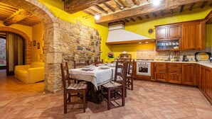 A rustic kitchen with stone walls, wooden cabinets, and a dining area with a table set for four. - Villa "Podere Spagliarda" with Private Pool, Terrace & Wi-Fi (San Quirico d'Orcia)