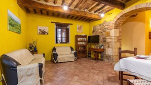 A room with a yellow wall, a stone wall, a wooden ceiling, a sofa, a chair, a table, and a television. - Villa "Podere Spagliarda" with Private Pool, Terrace & Wi-Fi (San Quirico d'Orcia)