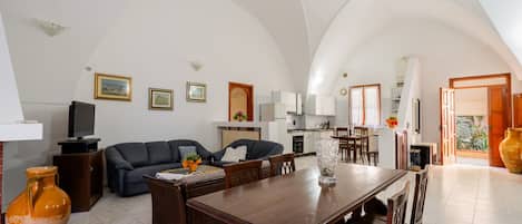 A spacious living area with a dining table, sofas, and a kitchen in the background.