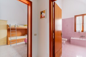 A room with a bunk bed, a wooden wardrobe, a bathroom with a bathtub, and a toilet.