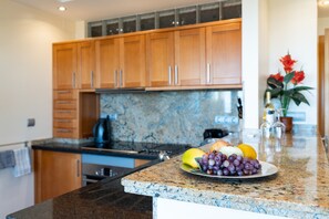 A kitchen with granite countertops, wooden cabinets, and a fruit bowl with grapes and citrus fruits.