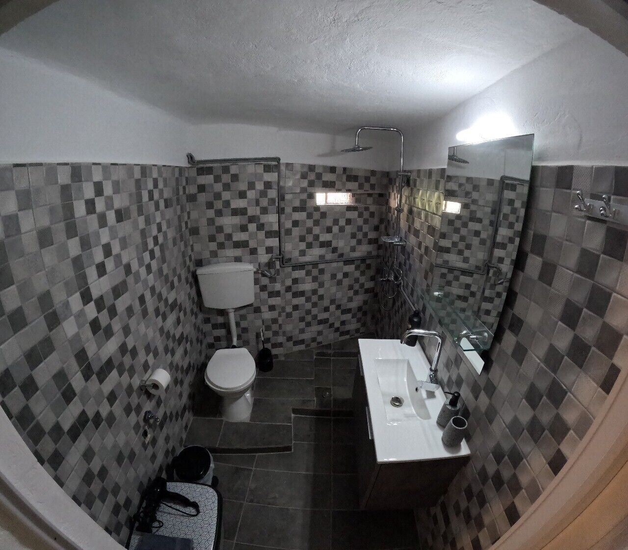 Un baño con pared de baldosas a cuadros, inodoro, lavamanos y ducha.