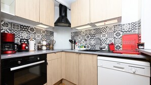 Een keuken met een patroon op de achterwand, een rode waterkoker, een koffiezetapparaat, een vaatwasser en een fornuis.