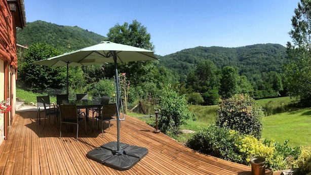 Een houten terras met buitenmeubilair, een tafel en een parasol.