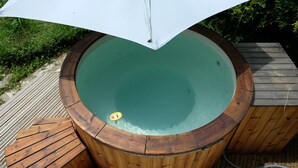 Een jacuzzi met een houten terras en een witte parasol.