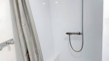 A shower with a handheld showerhead, a drain, and a curtain.