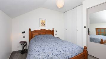 Una camera da letto con un letto in legno, un comodino, una lampada a parete, un quadro e una porta con uno specchio.