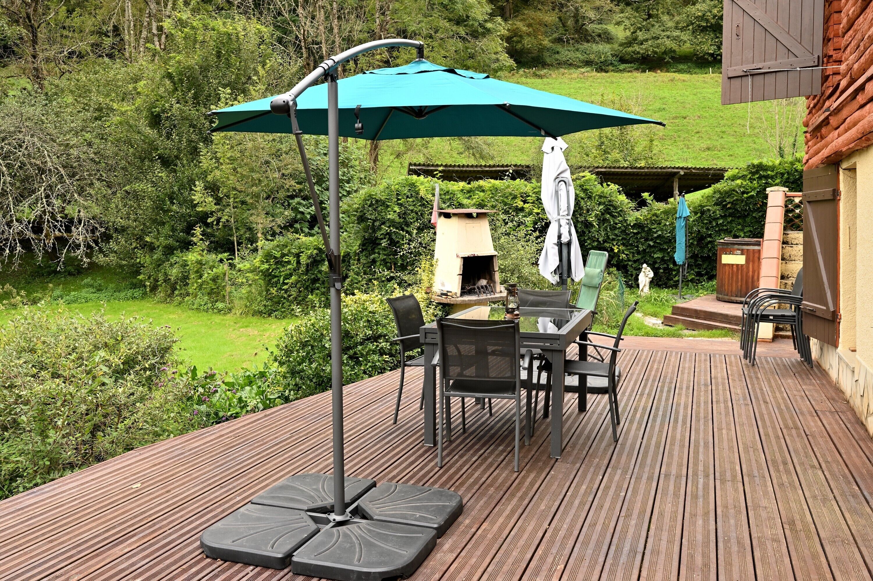 Une terrasse en bois avec une table et des chaises, un parasol vert et une petite maison pour chat.