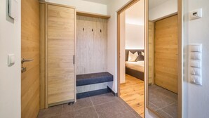 A room with a wooden wardrobe, a bench, a bed with pillows, and a tiled floor.