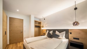 A modern bedroom with a wooden door, a bed with white linens, a headboard with built-in shelves, and a hanging pendant light.